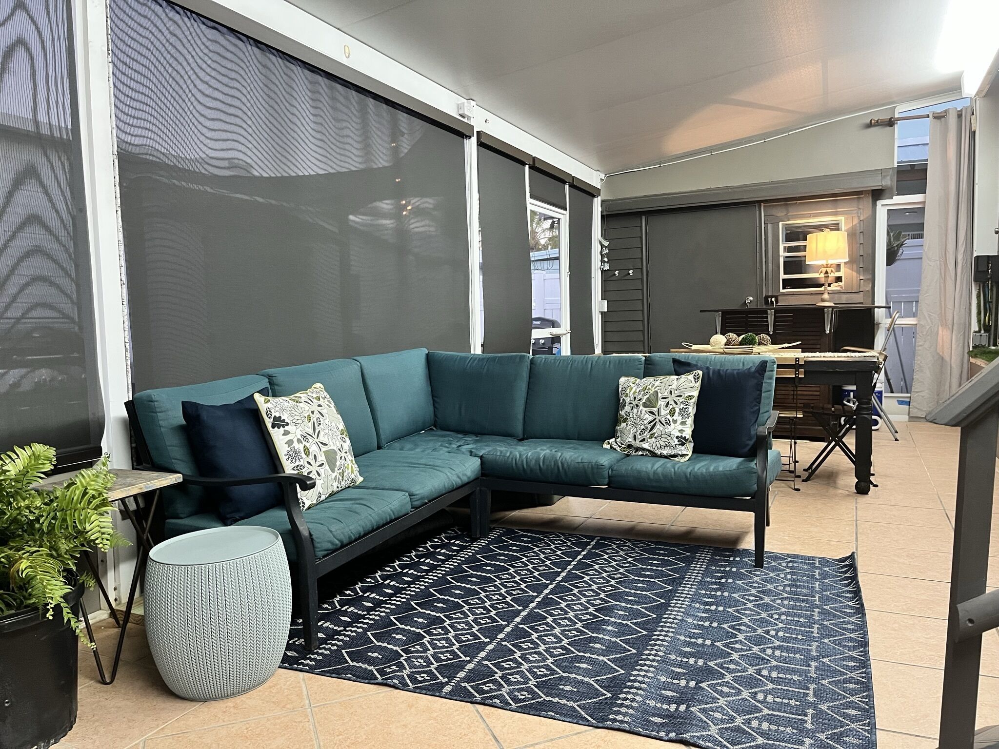 A modern living room with a teal sectional sofa, patterned cushions, a woven rug, and a potted plant.