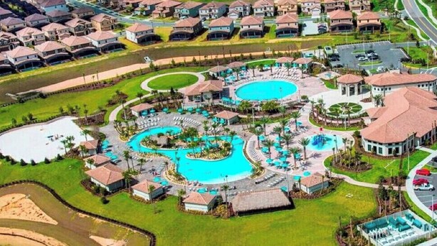 Et resort med flere swimmingpools, en central pavillon og en parkeringsplads.