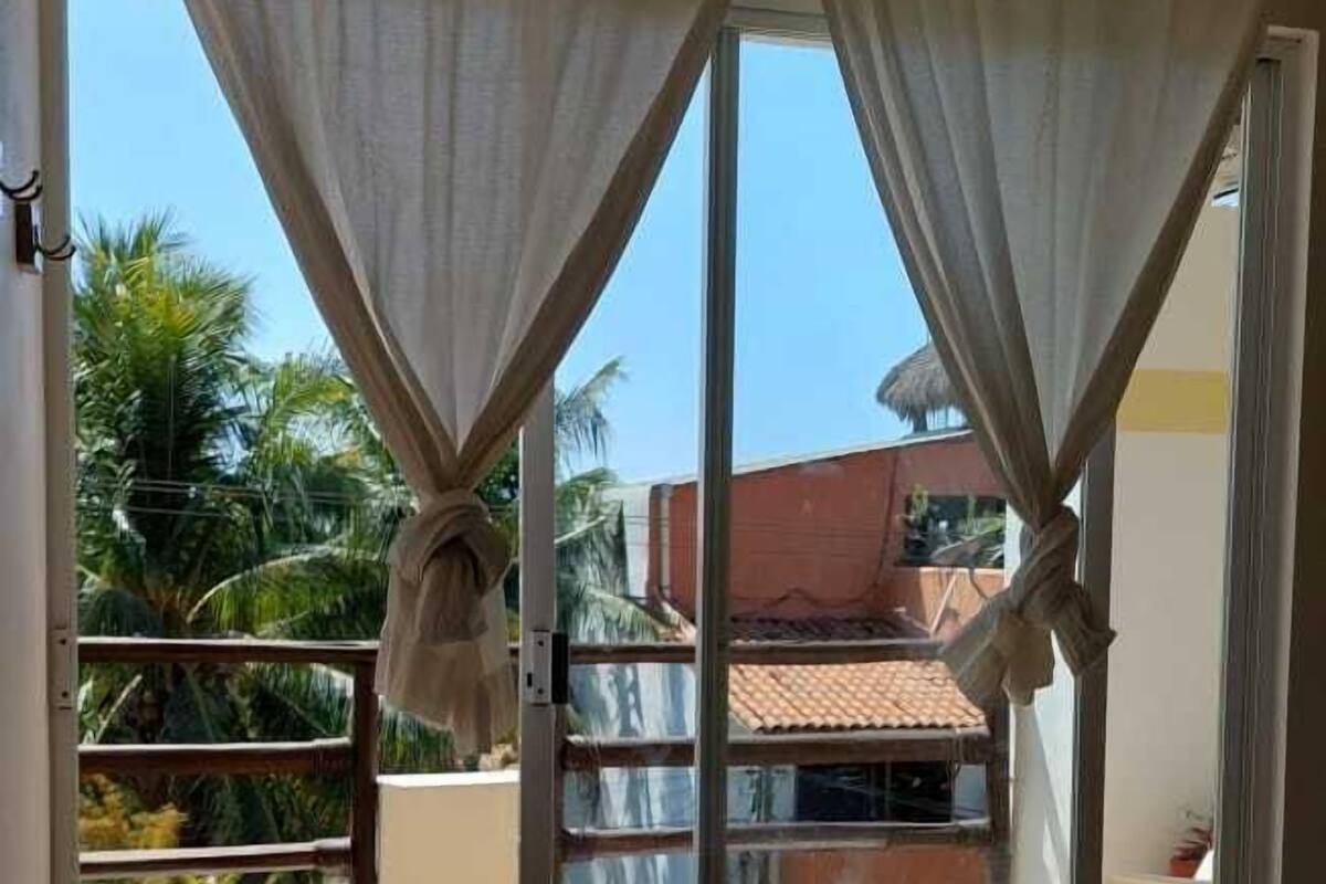 Ein Zimmer mit einer Schiebeglastür, die auf einen Balkon führt, Vorhängen, einer Bank und einer Klimaanlage.