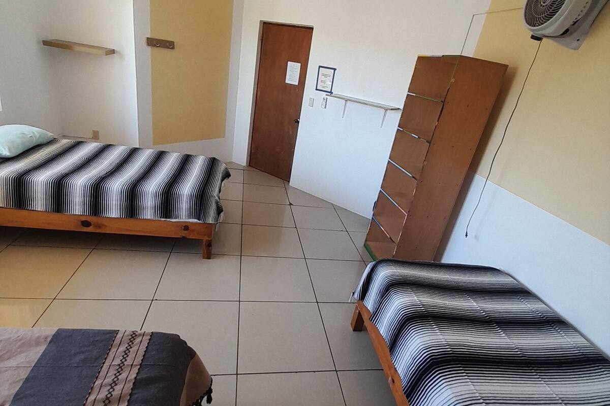 Ein Zimmer mit zwei Betten, einer Holztür, einer weißen Wand und einem Deckenventilator.