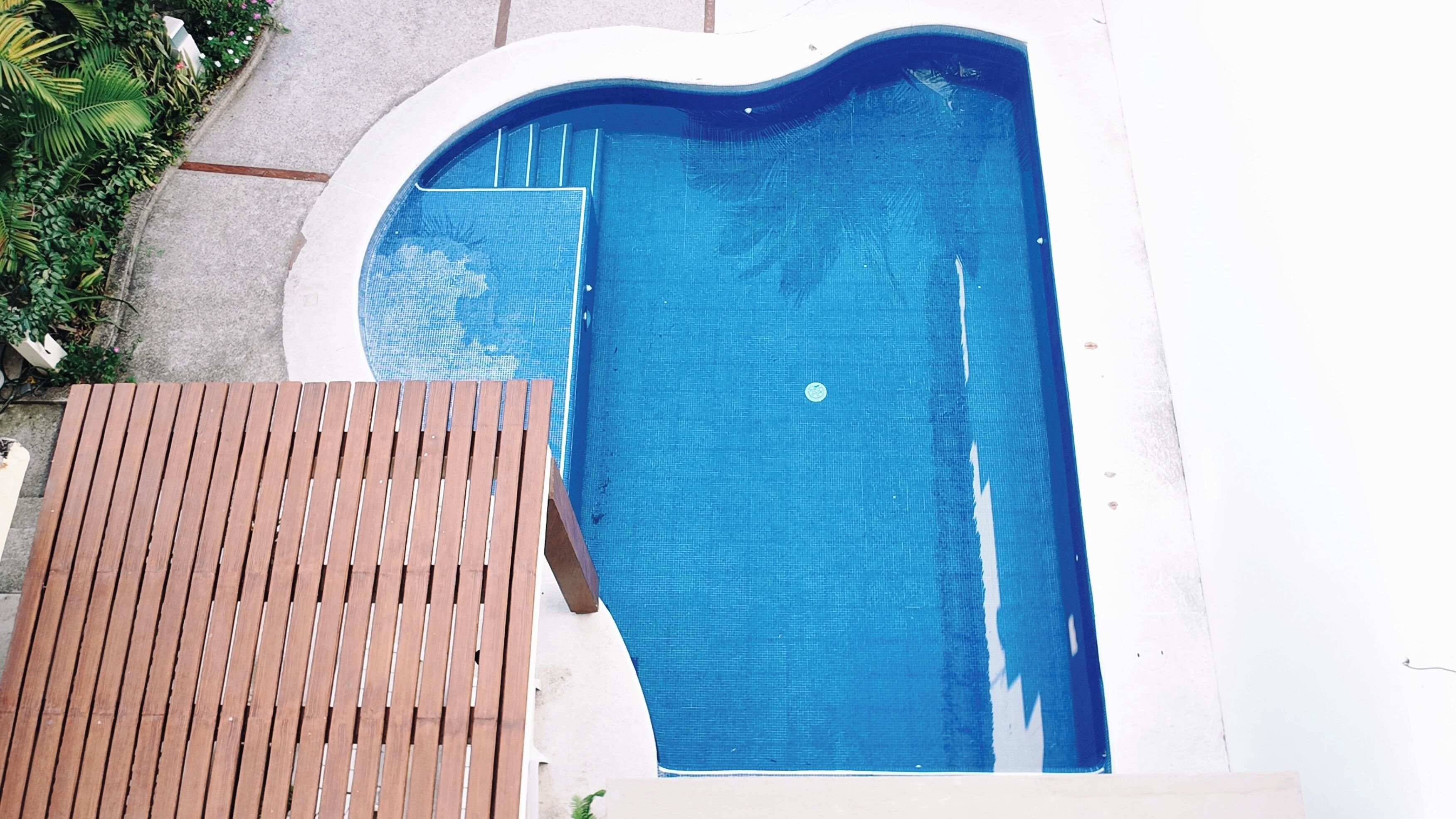 A swimming pool with a wooden deck and a white wall.