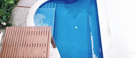 A swimming pool with a wooden deck and a white wall.