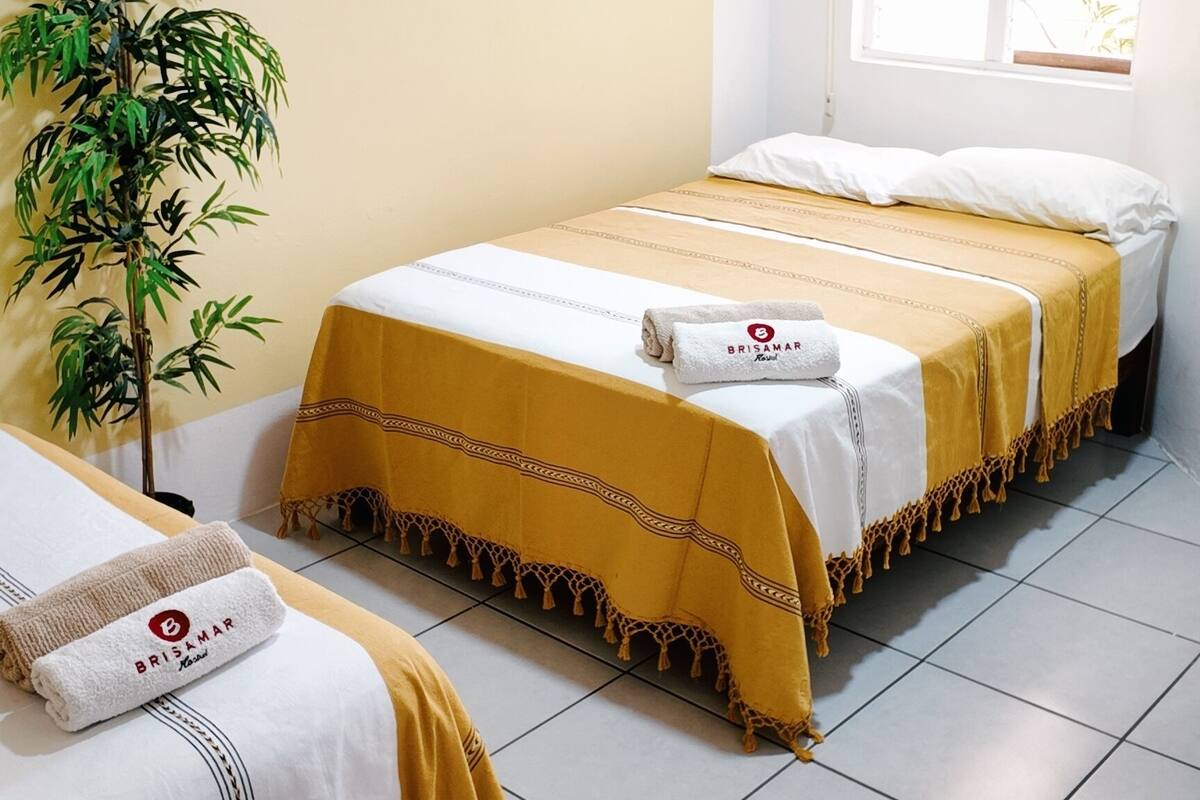 Ein Hotelzimmer mit zwei Betten, einem Blumentopf, einem Fenster und einer Klimaanlage.