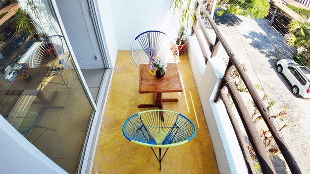 A balcony with a wooden table, two blue chairs, and a potted plant. - Brisamar Guesthouse (Puerto Escondido)
