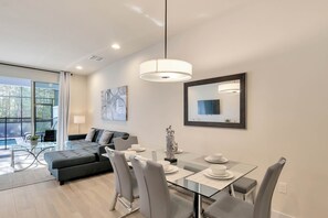 Un comedor moderno con una mesa de vidrio, sillas tapizadas de color gris y una lámpara colgante.