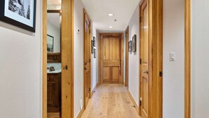 A hallway with wooden doors, a white wall, and a wooden floor.