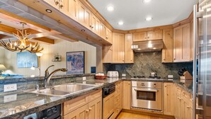 A kitchen with wooden cabinets, stainless steel appliances, a granite countertop, and a chandelier.