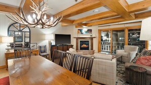 A spacious living area with a large wooden dining table, comfortable seating, a fireplace, and a modern chandelier.