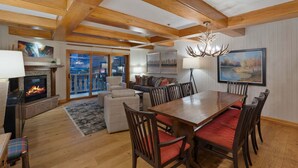 A spacious living room with a fireplace, a dining table with chairs, and a large window with a view.