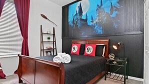 Ein Schlafzimmer mit einem Bett, roten Kissen, einem Nachttisch mit einer Lampe und einem Wandbild eines Schlosses.
