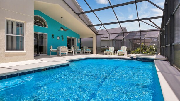 Ein Hallenbad mit klarem, blauem Wasser, umgeben von Liegestühlen und einer überdachten Terrasse.
