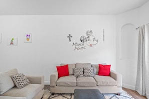 A living room with a beige sofa, red and grey cushions, and a wall decal of Mickey Mouse.