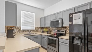 A modern kitchen with grey cabinets, a stainless steel refrigerator, a microwave, an oven, and a coffee maker. - RP144BD - Disney Regal Palms Townhome near Disney - Come on by! (Davenport)