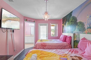 A bedroom with pink walls, two beds with matching bedding, a chandelier, a TV on the wall, and a mural of a castle.