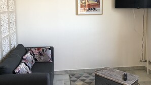 Een woonkamer met een bank, twee ingekaderde foto's, een televisie en een kamerkleed met een patroon.