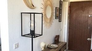 Een gang met een houten bank, een wandspiegel, een decoratieve zonneslinger spiegel en een lijst met een afbeelding.