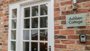 Un mur de briques avec une porte blanche et une enseigne indiquant « Ashben Cottage ».