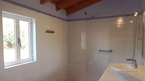 A bathroom with a shower, a sink, a window, and a wooden ceiling.