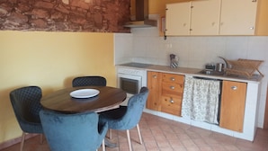 A compact kitchen with a dining area, featuring a stone wall, a stove, a sink, and wooden cabinets.
