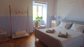 A bedroom with a bed, bedside tables, a hanging clothes rack, a potted plant, and a window with a view.