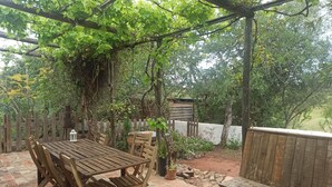 An outdoor patio with a wooden table and chairs, surrounded by a wooden fence and greenery.