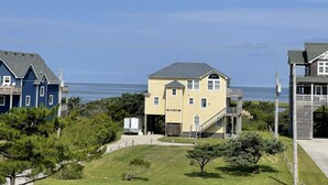 A coastal building with a yellow facade, a staircase leading to a deck, and a view of the ocean. - Swinkels is a spacious 3 bedroom, 1.5 bath home that is a true jewel! (FRISCO)