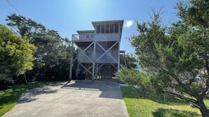 A modern multi-level wooden structure with a balcony, surrounded by greenery. - Swinkels is a spacious 3 bedroom, 1.5 bath home that is a true jewel! (FRISCO)