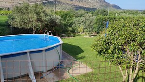 Une piscine hors sol, équipée d’une échelle, entourée d’une cour clôturée, agrémentée d’une végétation luxuriante et offrant une vue sur un paysage montagneux.