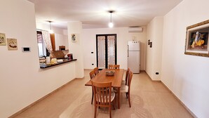 Un coin repas avec une table et des chaises en bois, une cuisine à l’arrière-plan et un tableau encadré au mur.