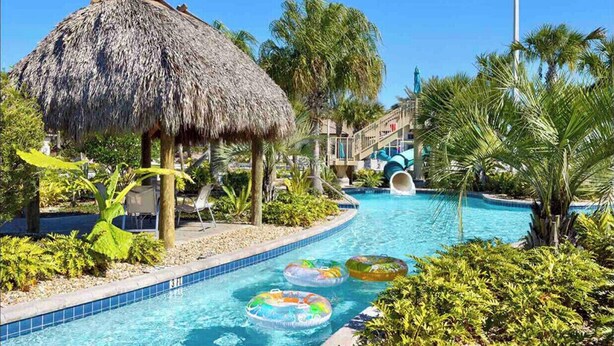 A swimming pool with a thatched-roof structure, palm trees, and inflatable rings. - 7BR Champions Gate Resort/Private Pool & Spa/15 min to Disney/Sleeps 16+ (Davenport)