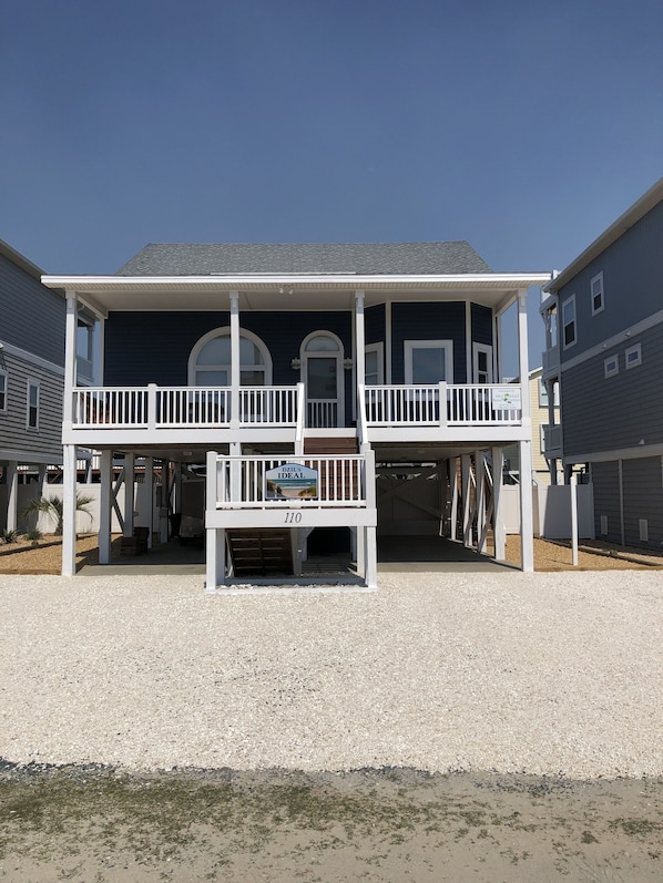 A two-story house with a covered porch, a front door, and a sign indicating it is for sale. - Pet friendly Beach House with a Heated Pool. (Holden Beach)