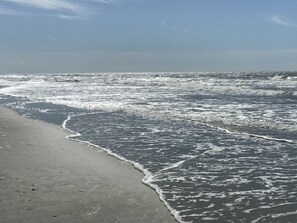 A beach with waves gently lapping onto the shore. - Pet friendly Beach House with a Heated Pool. (Holden Beach)