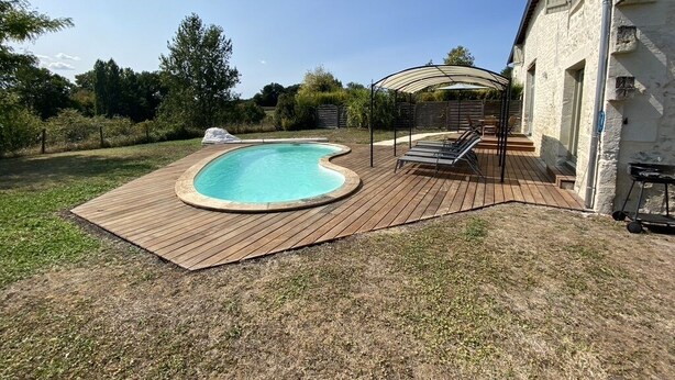 A backyard with a swimming pool, wooden deck, and a covered seating area. - Les Houx - Old barn with private swimming pool (Chalais)
