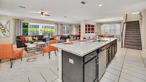 A modern kitchen with a central island, dining area with orange chairs, and a staircase leading to an upper level. - Avenger's, Frozen and Alice in Wonderland Themed Rooms! Private Pool and Modern Decor! (Kissimmee)