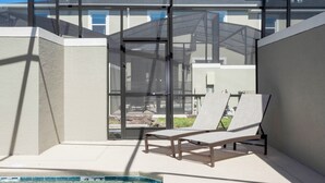 Ein überdachter Außenbereich mit zwei Liegestühlen und einem Pool.