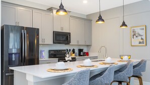 Eine moderne Küche mit Edelstahlgeräten, einer zentralen Kochinsel mit Barhocker, Pendelleuchten und einer Mikrowelle über der Insel.