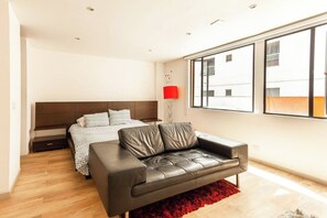Quarto moderno com cama, sofá de couro e uma janela grande.