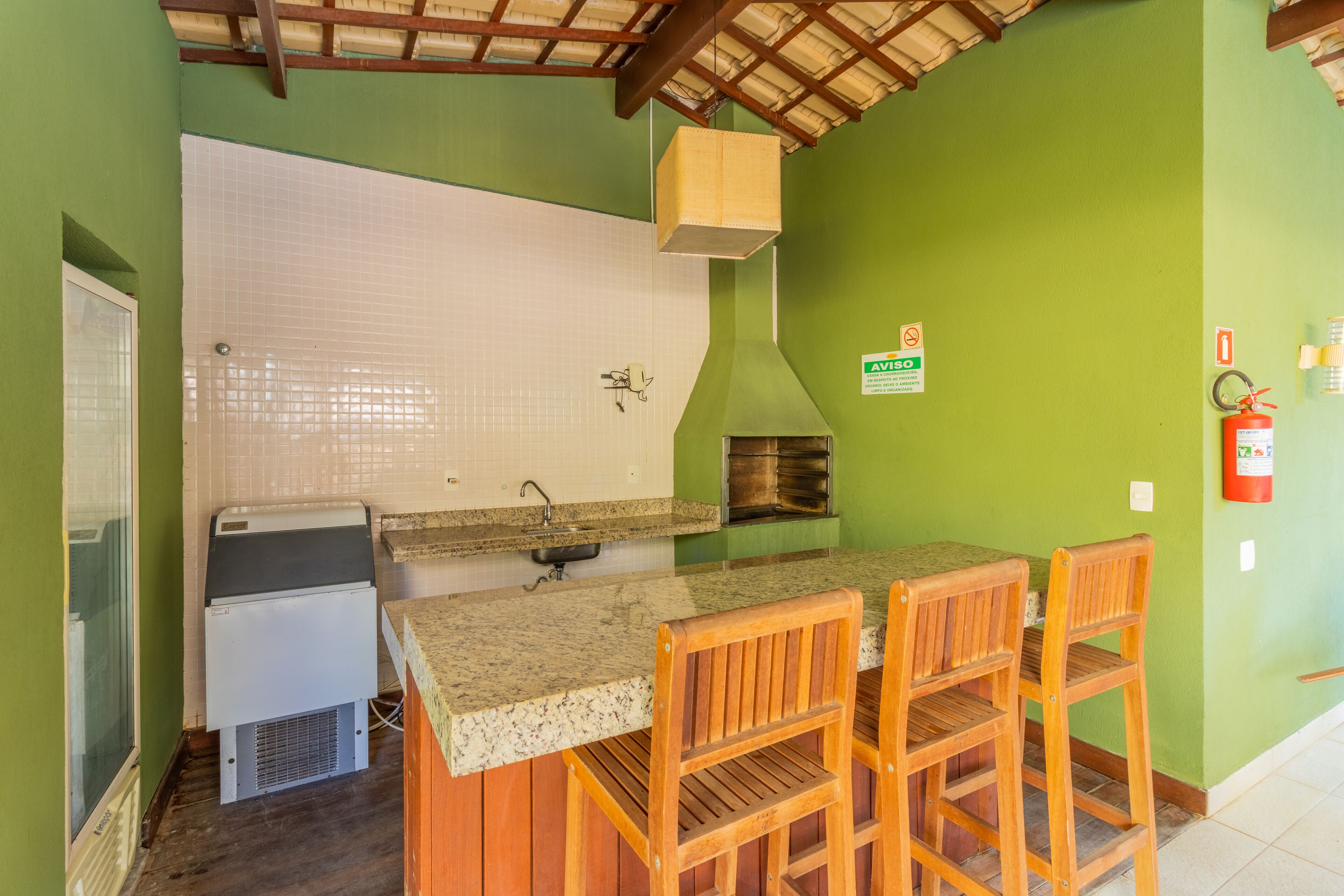 A kitchen with a granite countertop, wooden chairs, a white refrigerator, a tiled backsplash, and a green wall.