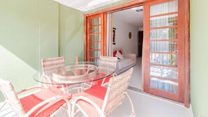 A glass-top table with wicker chairs, a white sofa, and a wooden door with glass panels. - PF36 Ótimo Quarto e Sala a 25m da Praia (Mata de São João)
