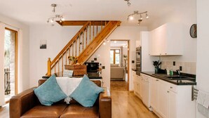 Eine moderne Küche mit weißen Schränken, einer Holztreppe und einem Ledersofa mit blauen Kissen.