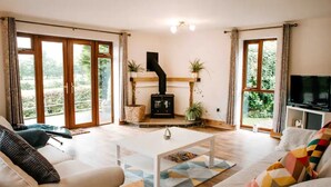 Ein Wohnzimmer mit Kamin, großen Fenstern und einem Fernseher.