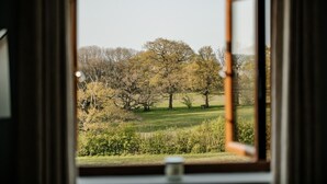 Blick aus einem Fenster mit Holzrahmen auf ein grünes Feld mit Bäumen.