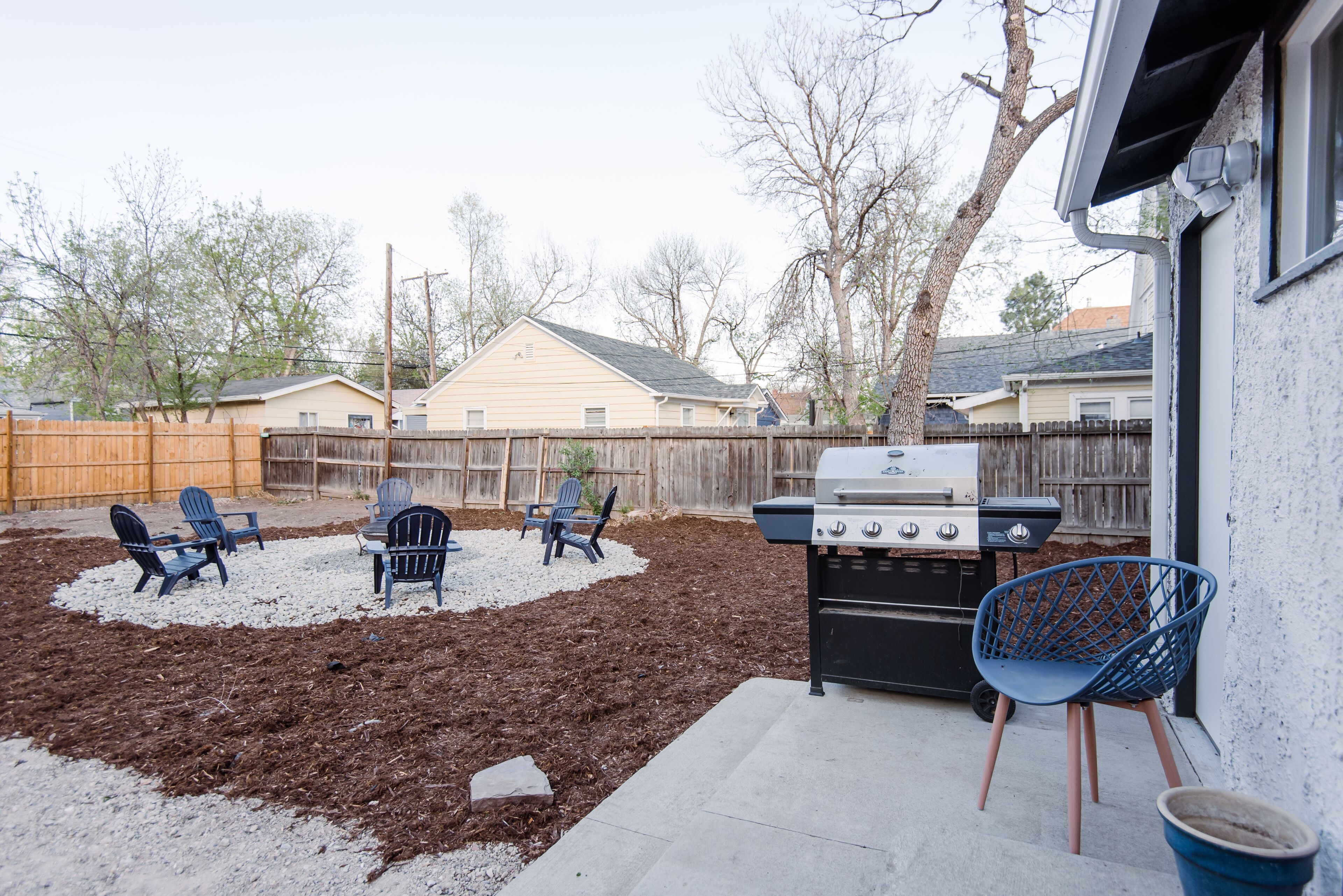 A backyard with a barbecue grill, outdoor chairs, and a wooden fence.