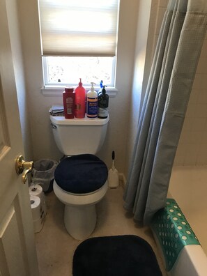 A small bathroom with a toilet, a window with blinds, a shower curtain, and toiletries on the toilet tank. - Nice bedroom and bath in large 2 story house (Centennial)