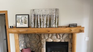 Une cheminée en pierre avec un poêle à bois noir, une cheminée en bois et un tableau encadré au-dessus.