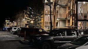 Une rangée de voitures garées le long d’une rue bordée d’immeubles à plusieurs étages, dotés de balcons et de garde-corps.