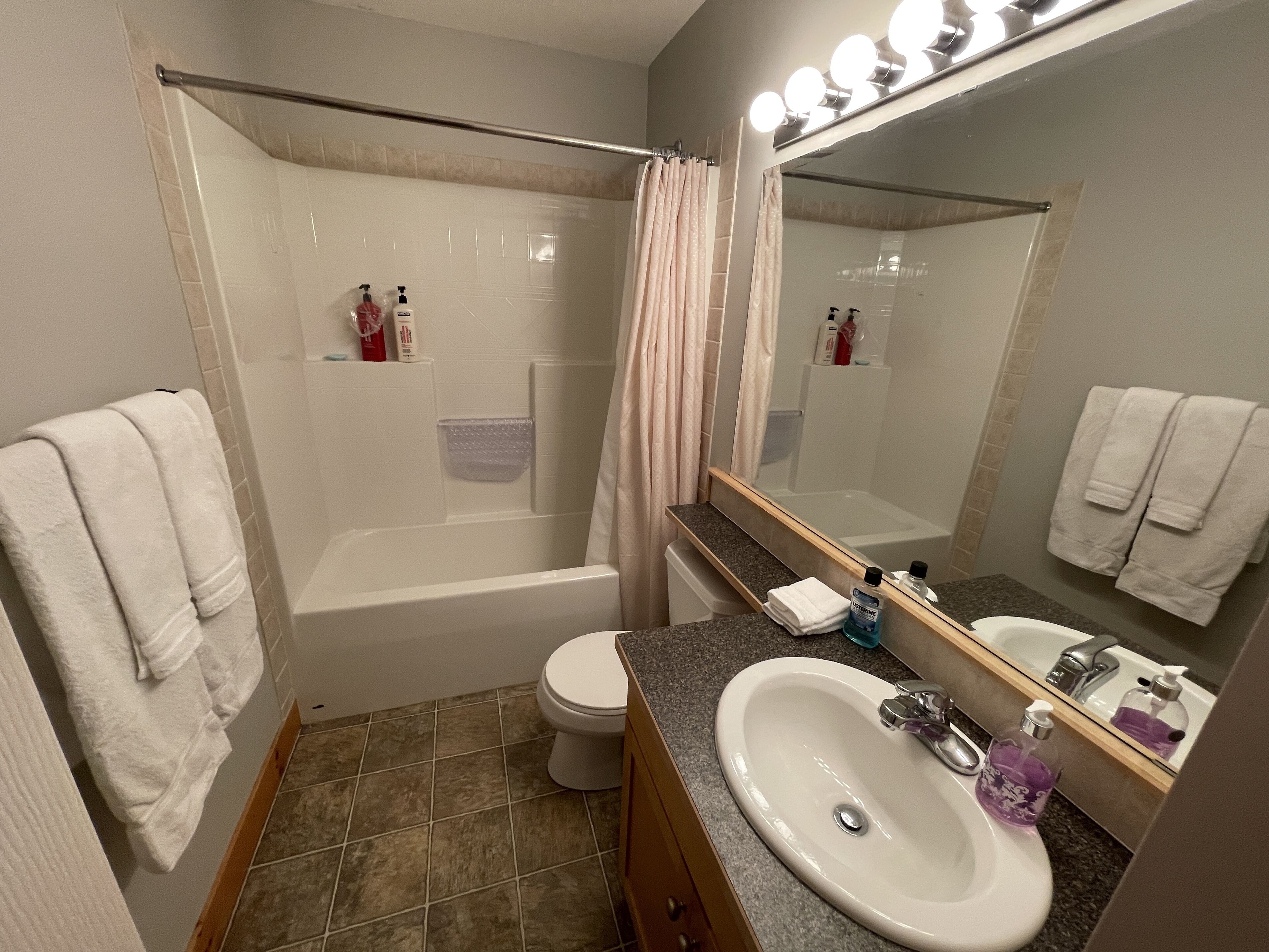 Een badkamer met een bad, toilet, wastafel en een grote spiegel met verlichting.