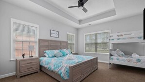 Un dormitorio con una cama grande, una mesita de noche, un aparador, un ventilador de techo y una cama litera.