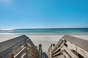 A wooden boardwalk leading to a sandy beach with a clear blue sky.