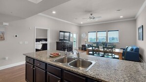 Una cocina moderna con encimeras de granito, pileta de acero inoxidable y muebles oscuros. Hay un comedor con mesa de madera y sillas azules.